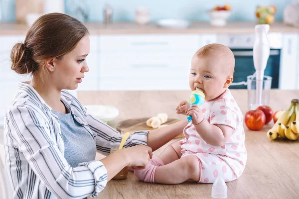 Mother feeding her little baby in kitchen at home — Stock Photo, Image