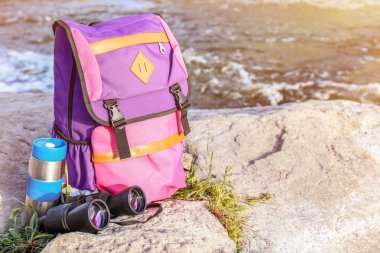 Dağ akımına yakın kaya üzerinde termos ve binoküler ile turist sırt çantası