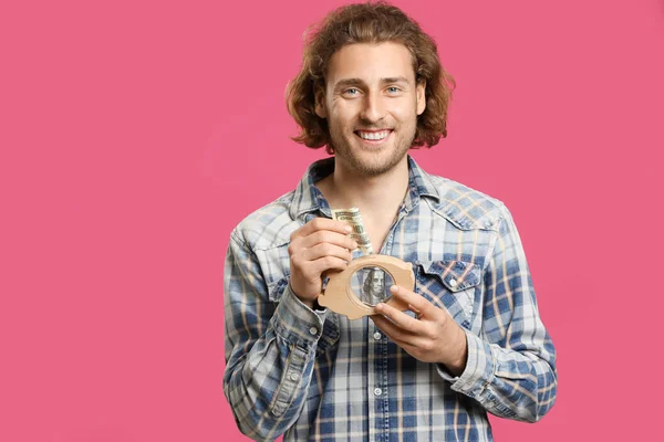 Handsome man with money and piggy bank on color background — Stock Photo, Image