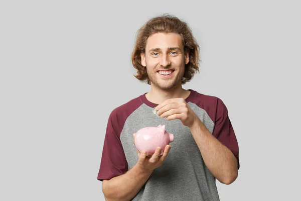Handsome man with piggy bank on grey background — Stock Photo, Image
