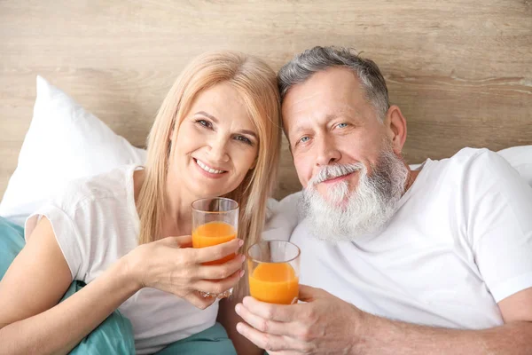 Happy elderly couple drinking juice in bed — Stock Photo, Image