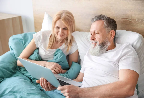 Feliz pareja de ancianos con portátil descansando en la cama —  Fotos de Stock