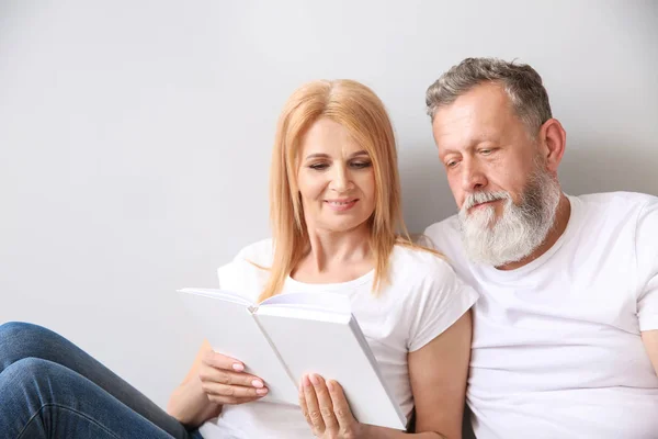 Hermosa pareja de ancianos leyendo libro sobre fondo claro —  Fotos de Stock