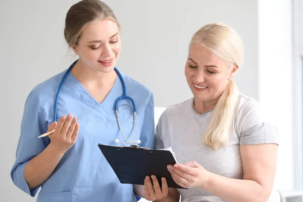 Assistente medico spiegando donna matura la sua diagnosi in clinica — Foto Stock