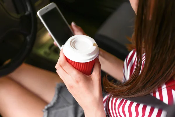 Young woman with mobile phone and coffee in car, closeup