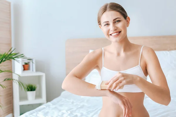 Beautiful young woman epilating arms at home — Stock Photo, Image