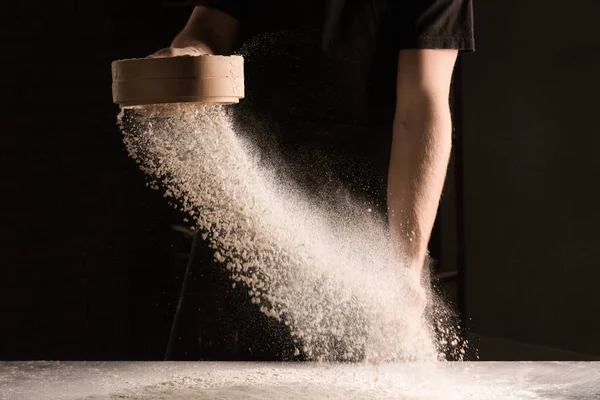 Man sieving flour on dark background