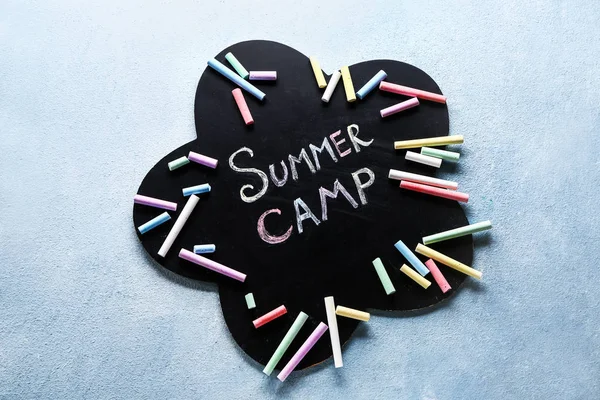 Chalkboard with text SUMMER CAMP and crayons on color background