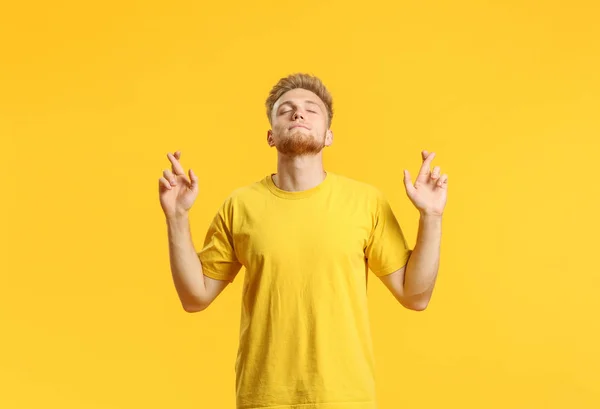 Portrait of handsome young man with crossed fingers on color background — Stock Photo, Image