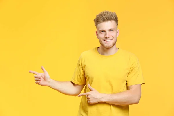 Portrait of handsome young man pointing at something on color background — Stock Photo, Image