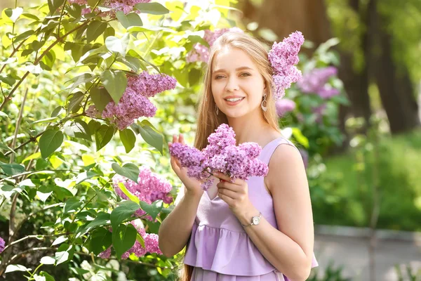 Güzel genç kadın yakın çiçek Lila Bush açık havada — Stok fotoğraf