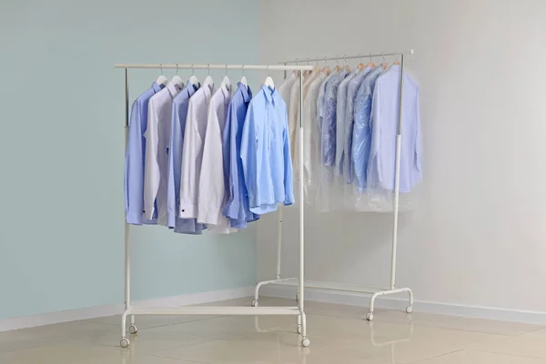 Rekken met kleren na het drogen-schoonmaken dichtbij lichte muur — Stockfoto
