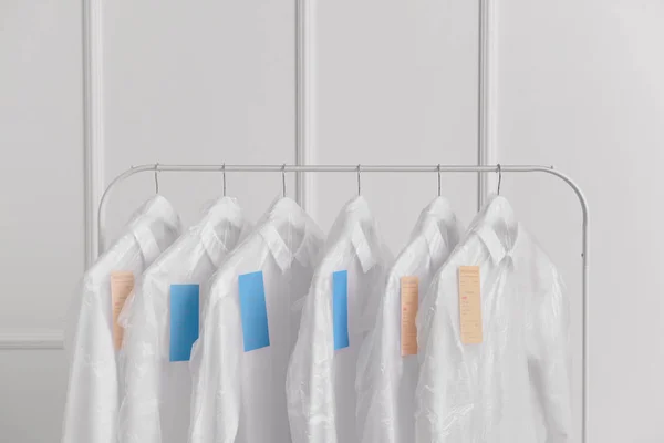 Cremalheira com roupas após a limpeza a seco perto da parede branca — Fotografia de Stock