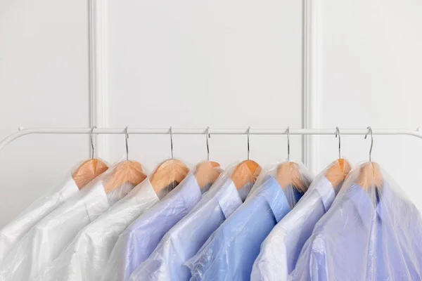 Rack with clothes after dry-cleaning near white wall — Stock Photo, Image