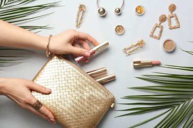 Hafif arka planda kozmetik çanta, aksesuar ve palmiye yaprakları ile kadın eller