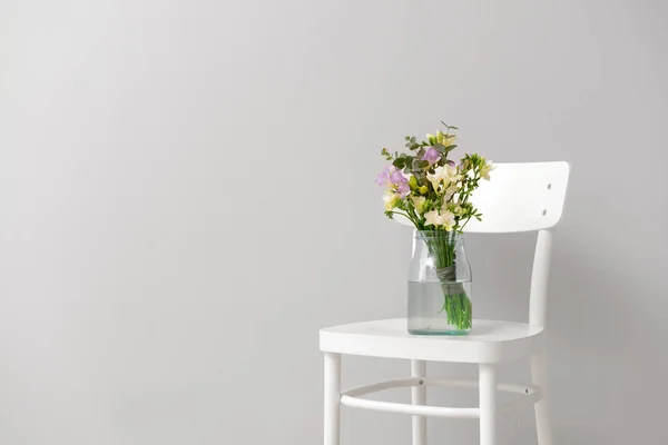 Vase with beautiful freesia flowers on chair against light background — Stock Photo, Image