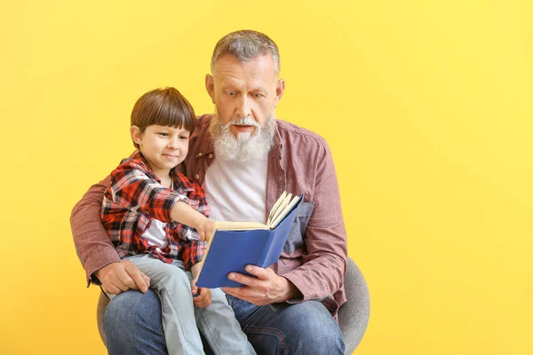 Lindo niño leyendo libro con el abuelo en el fondo de color — Foto de Stock