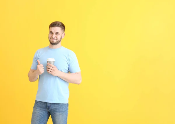 Knappe jonge man met kop koffie op kleur achtergrond — Stockfoto