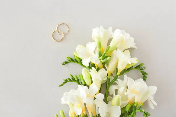 Vigsel ringar och vackra Freesia blommor på ljus bakgrund — Stockfoto