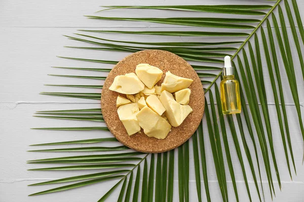 Cocoa butter, bottle of essential oil and palm leaf on table — Stock Photo, Image