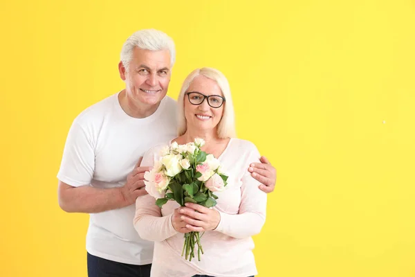Portrait of happy mature couple with flowers on color background — Stock Photo, Image