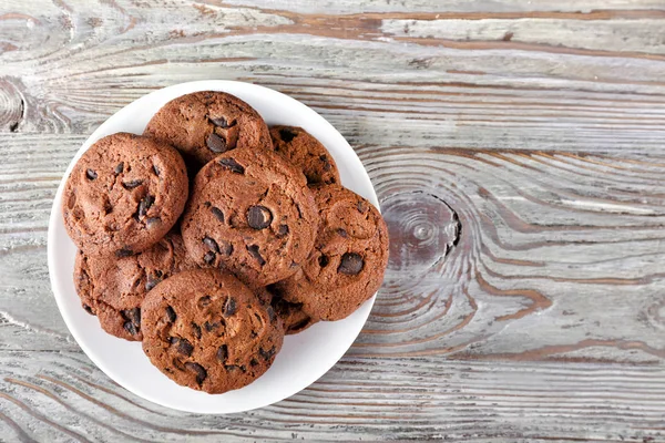 Piatto con gustosi biscotti al cioccolato sul tavolo di legno — Foto Stock