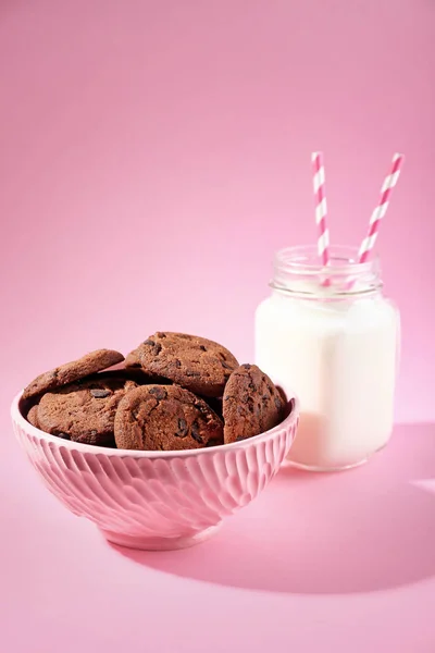 Cuenco con sabrosas galletas de chocolate y tarro de leche sobre fondo de color —  Fotos de Stock