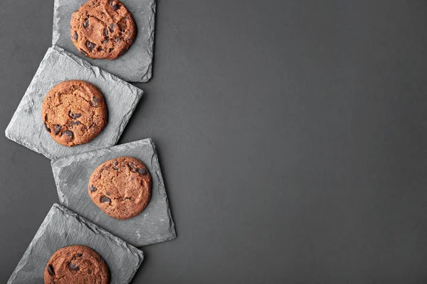 Piatti di ardesia e gustosi biscotti al cioccolato su sfondo scuro — Foto Stock