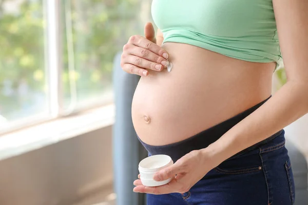 Junge schwangere Frau cremt sich zu Hause gegen Dehnungsstreifen am Bauch ein — Stockfoto
