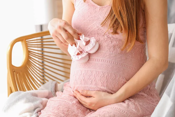 Jonge zwangere vrouw met baby laarzen thuis — Stockfoto