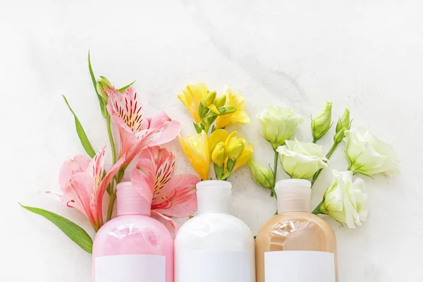 Bottles of shampoo and flowers on light background — Stock Photo, Image