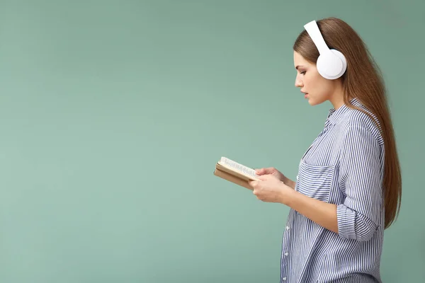 Young woman listening to music and reading book on color background — Stock Photo, Image