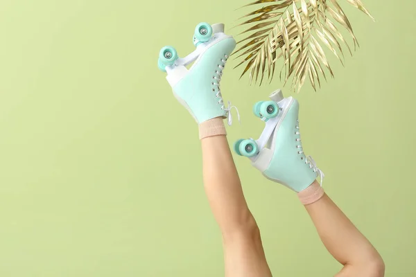 Legs of woman in roller skates and golden tropical leaves on color background — Stock Photo, Image