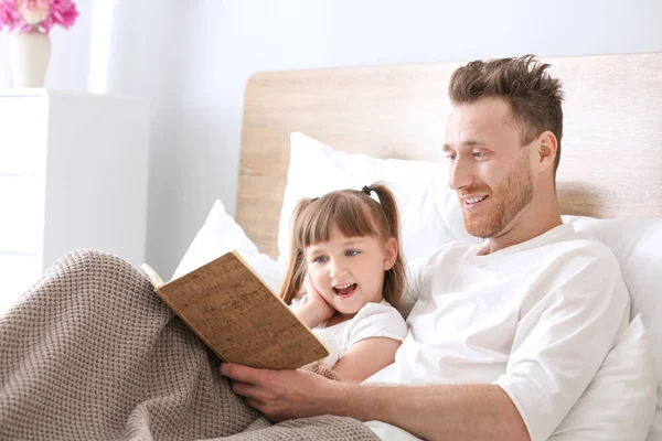 Vader en zijn kleine dochter lezen boek in bed — Stockfoto