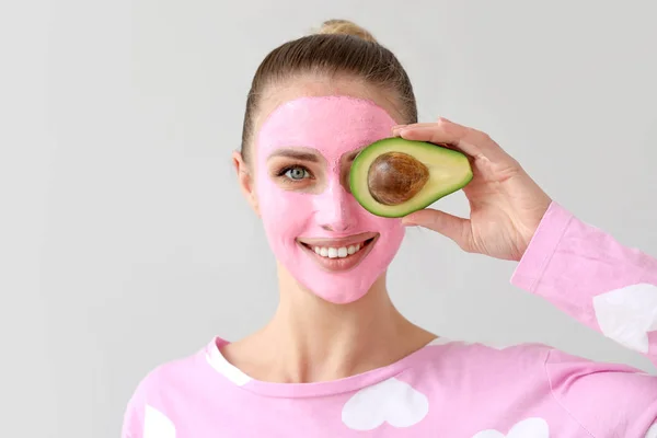 Beautiful young woman with facial mask and avocado on grey background — Stock Photo, Image