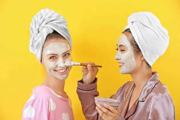 Wanita muda cantik menerapkan masker wajah dengan latar belakang warna — Stok Foto
