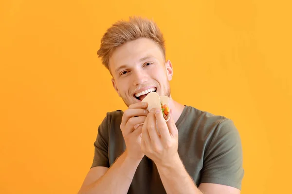 Hombre comiendo taco sabroso sobre fondo de color — Foto de Stock