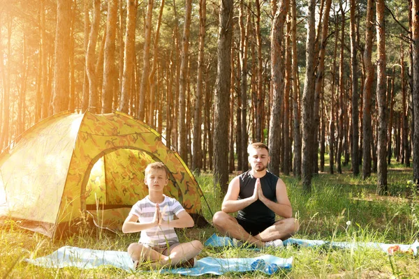 Padre e il suo piccolo figlio praticare yoga vicino tenda da campeggio nella foresta — Foto Stock