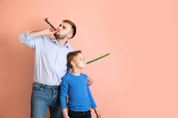 Padre y su hijito con silbatos de fiesta sobre fondo de color — Foto de Stock