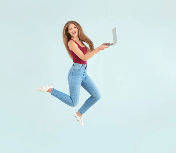 Beautiful jumping woman with laptop on color background — Stock Photo, Image