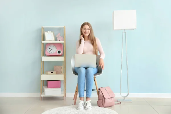 Beautiful young woman with laptop sitting on chair at home — Stock Photo, Image