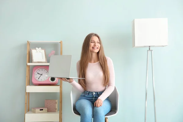 Mooie jonge vrouw met laptop zittend op de stoel thuis — Stockfoto