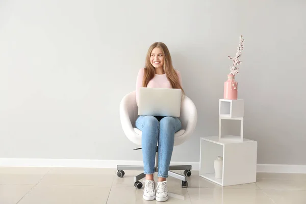 Beautiful young woman with laptop sitting on chair indoors — Stock Photo, Image