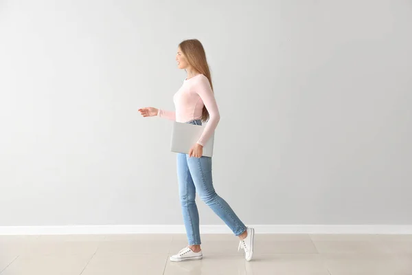 Beautiful young woman with laptop against light wall — Stock Photo, Image