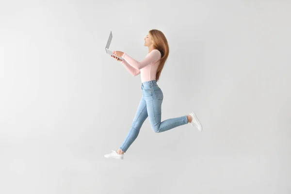 Jumping fiatal nő laptop-ra könnyű háttér — Stock Fotó