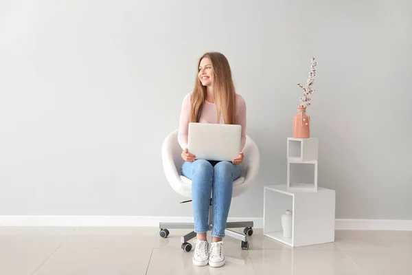 Vacker ung kvinna med laptop sitter på stolen inomhus — Stockfoto