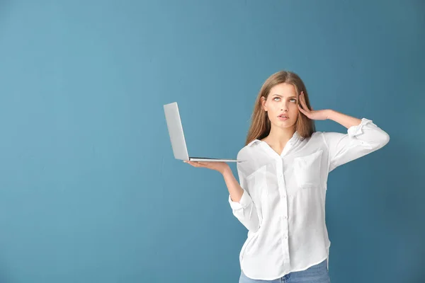 Mujer joven reflexiva con ordenador portátil en el fondo de color — Foto de Stock