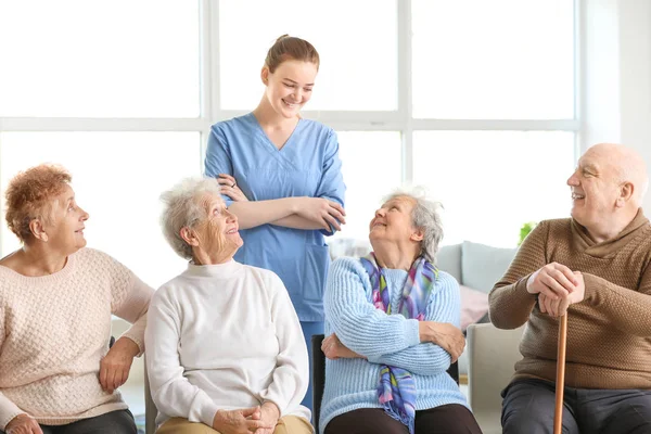 Young caregiver with group of senior people in nursing home — Stock Photo, Image