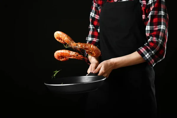 Mujer con sartén cocinando sabrosos camarones sobre fondo oscuro —  Fotos de Stock