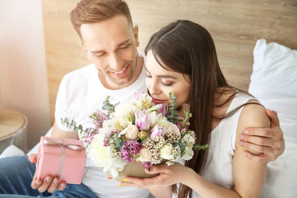 Marido saludando a su esposa con ramo de flores en el dormitorio en casa —  Fotos de Stock